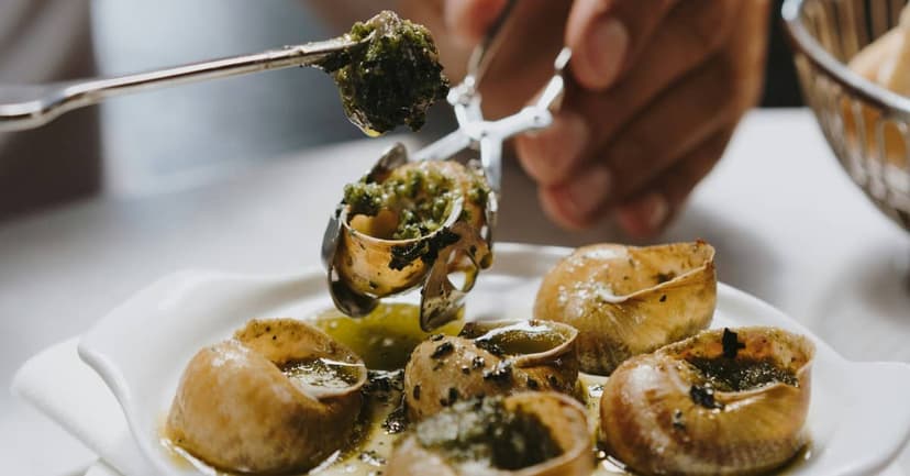 A plate of escargots in garlic and parsley butter being served with tongs