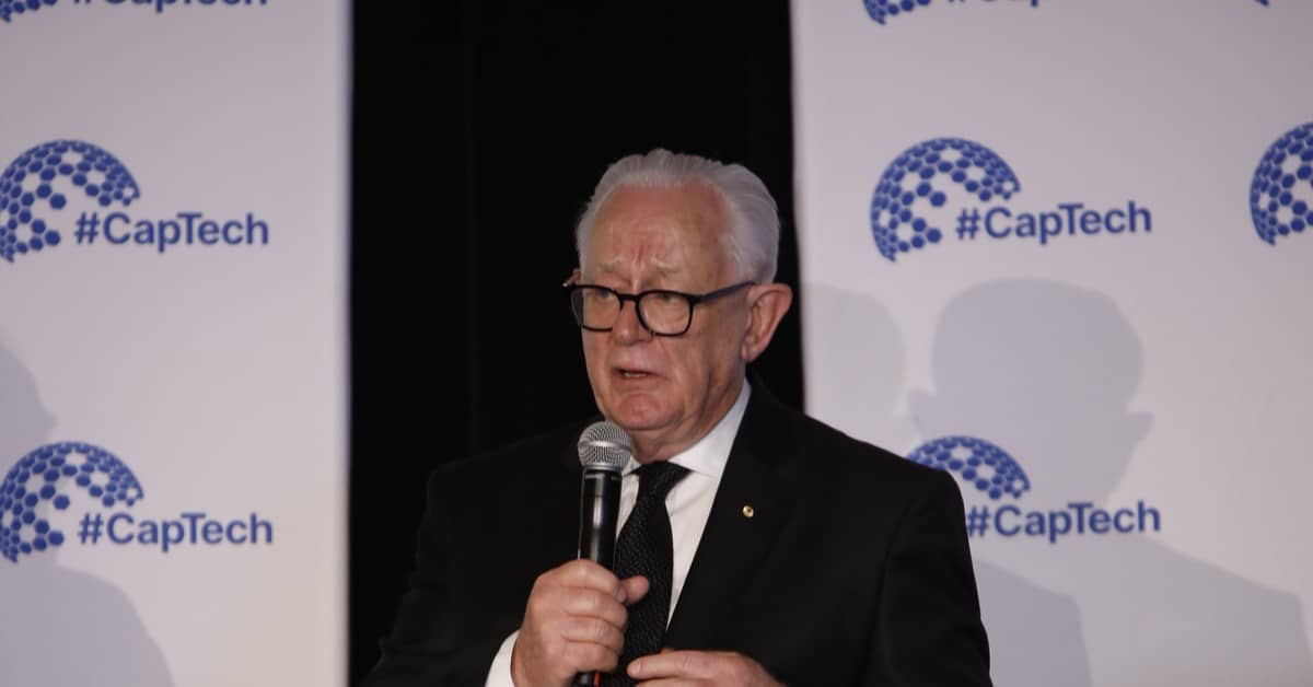 Andrew Robb speaking into a microphone on stage at the CapTech conference
