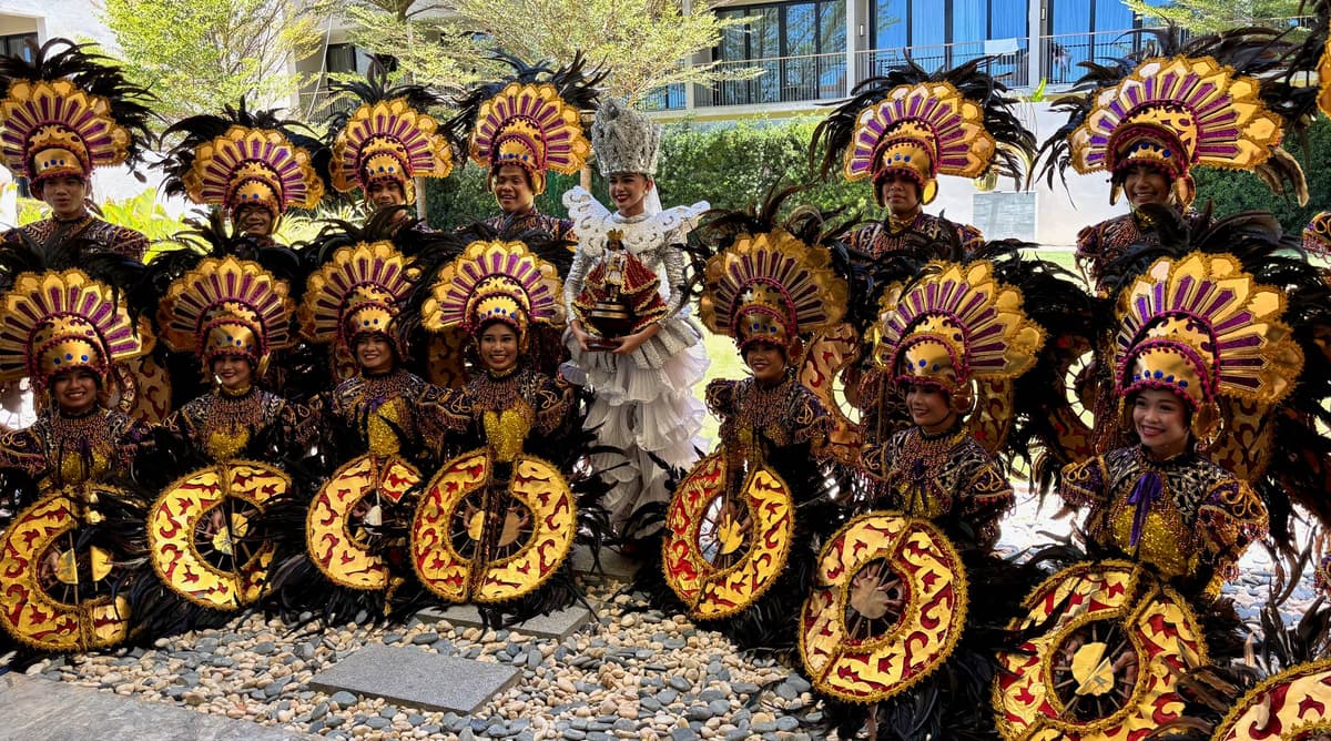 Sinulog festival dancers in gold and black feathered costumes around a performer holding the Santo Niño